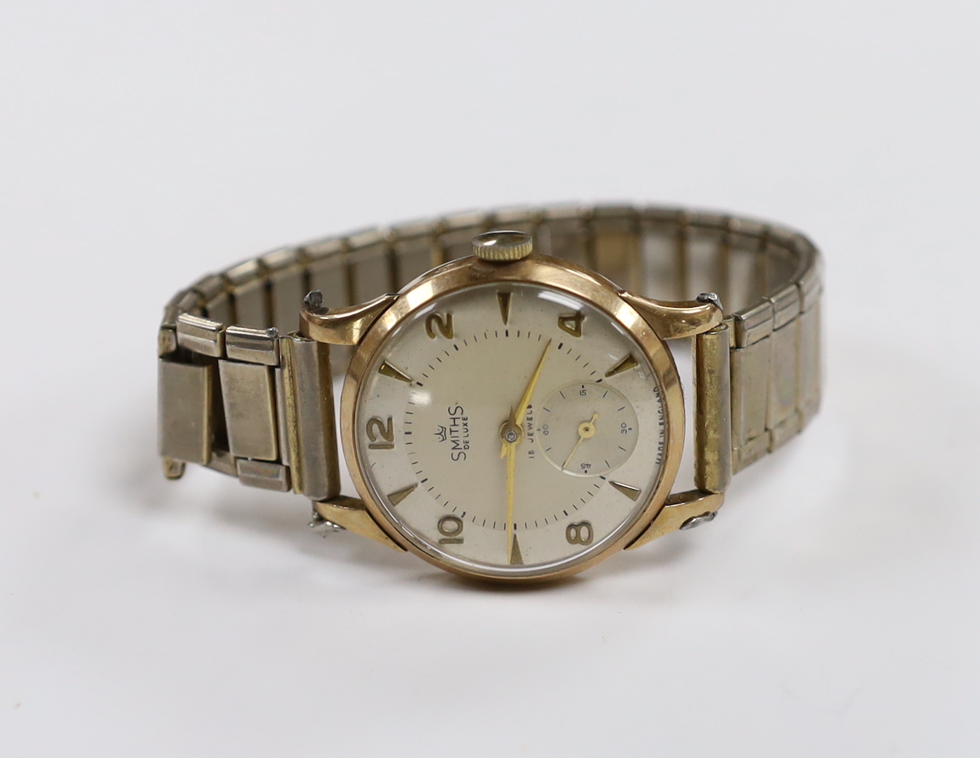 A gentleman's 9ct gold Smiths Deluxe manual wind wrist watch, with subsidiary seconds and case back inscription, on an associated flexible strap.